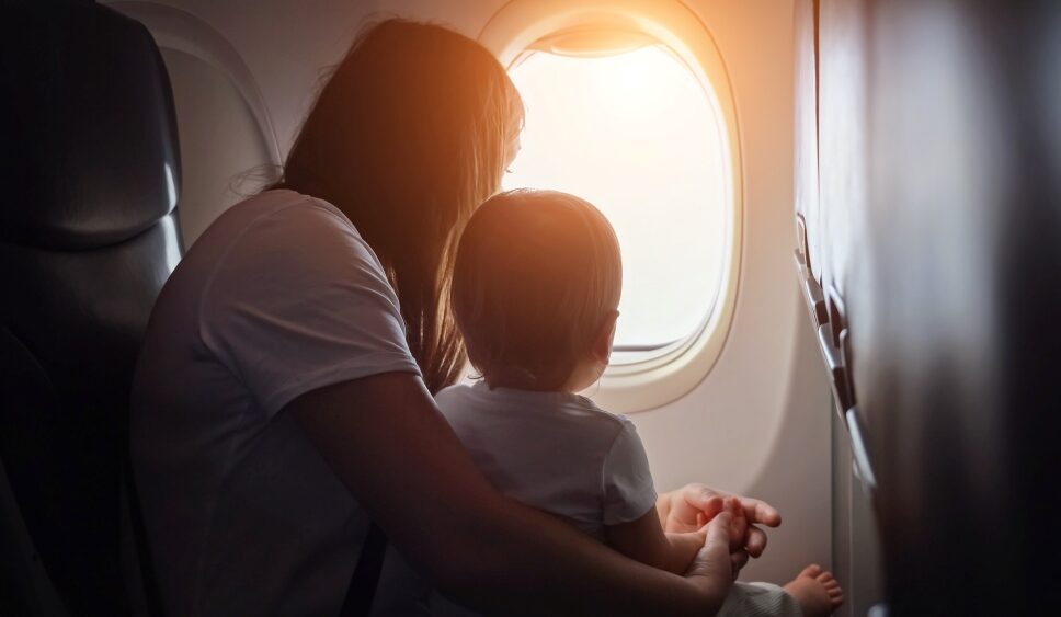 Joyful-mother-shows-view-from-plane-window-child-cradled-in-arms